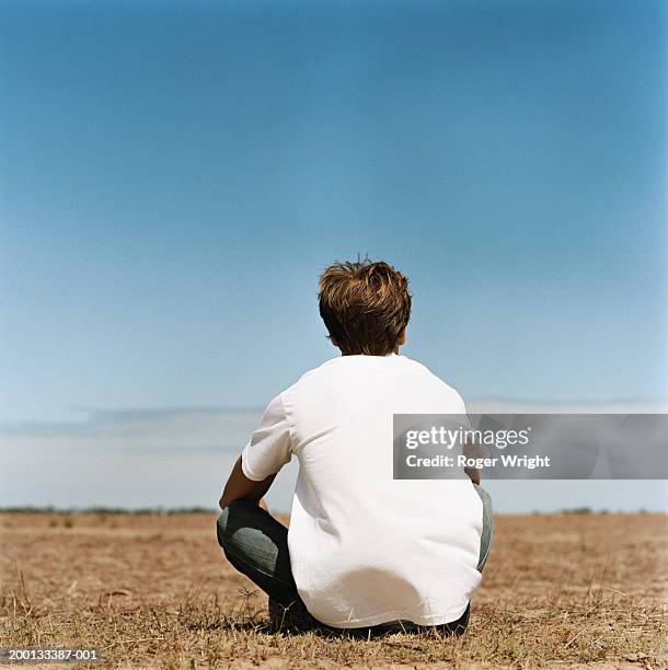 young man sitting cross legged in field, rear view - white t shirt bildbanksfoton och bilder