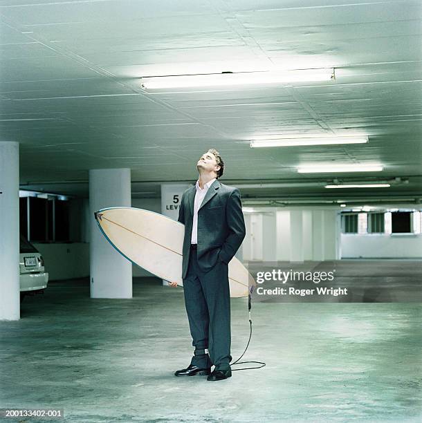 businessman in car park, holding surfboard, head raised, eyes closed - out of context ストックフォトと画像