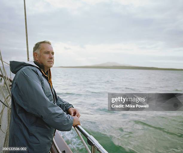 mature man leaning on railing of sailboat, looking out at sea - boat side view stock pictures, royalty-free photos & images