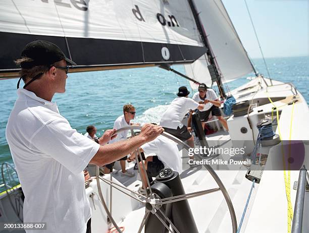 man standing at helm, sailing ocean going racing yacht, rear view - sailing team stock-fotos und bilder