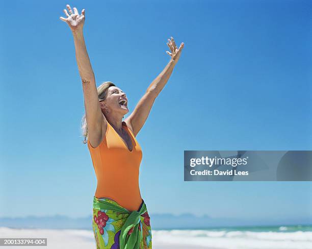 mature woman on beach, arms raised - sarong stock-fotos und bilder