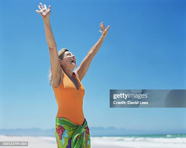 mature woman on beach, arms raised - middle aged woman bathing suit stock pictures, royalty-free photos & images