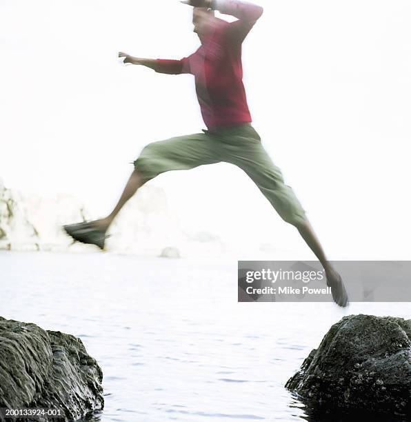 young man jumping between rocks (blurred motion) - bridge building stockfoto's en -beelden