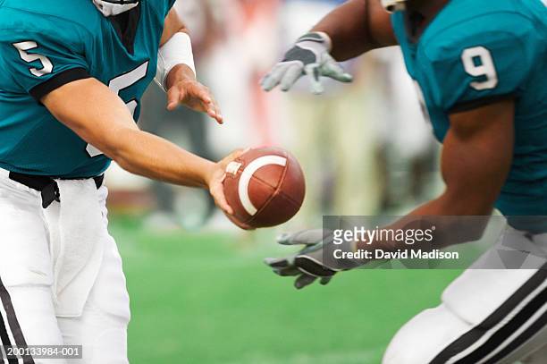 quarterback handing off football to running back, mid section - pasar fotografías e imágenes de stock