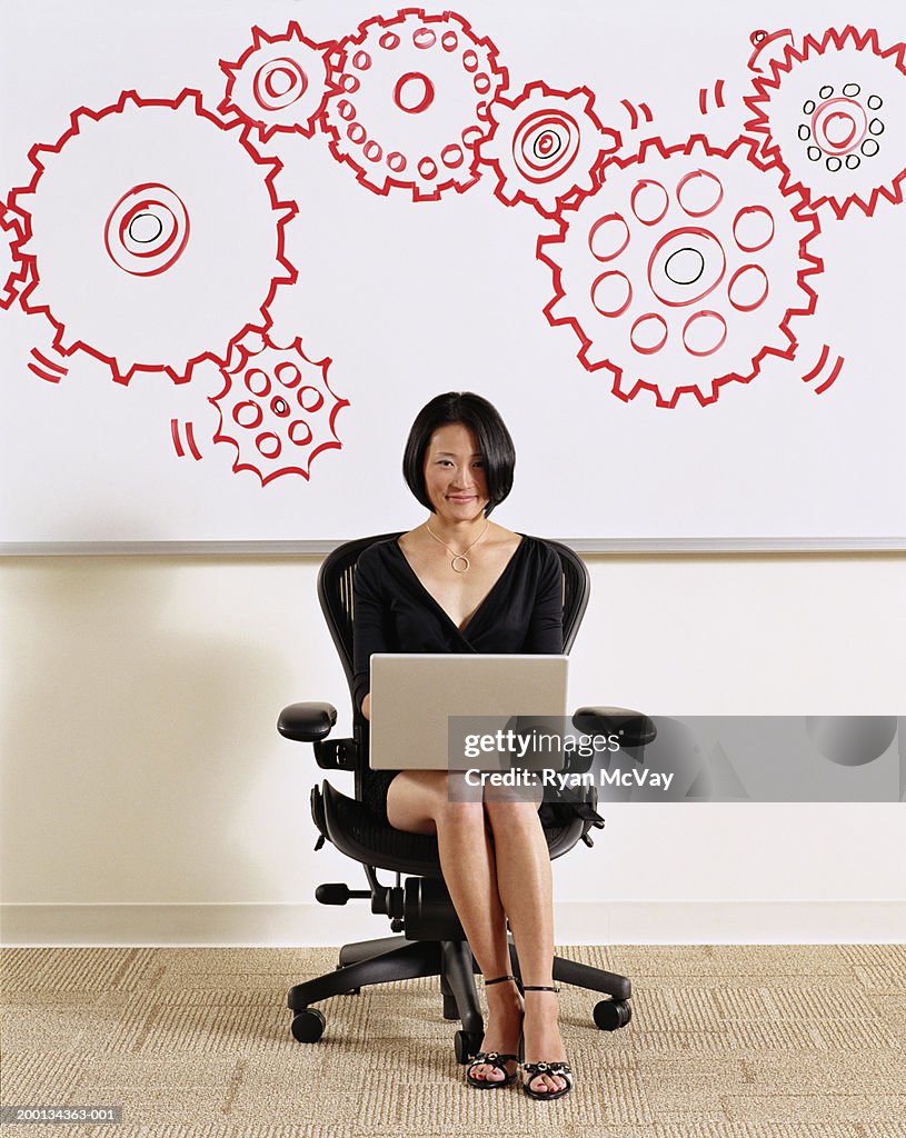 Woman using laptop, illustrated cogs on whiteboard in background