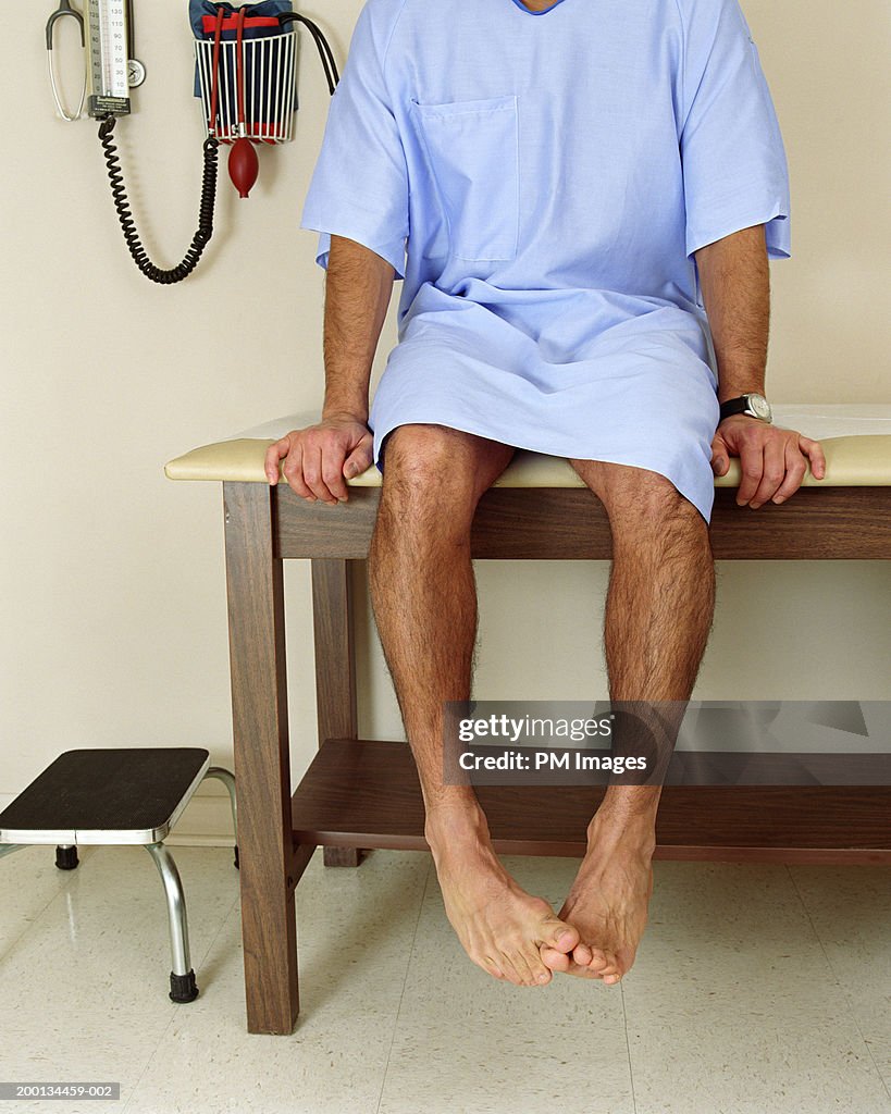 Male patient sitting on examining room table, mid section