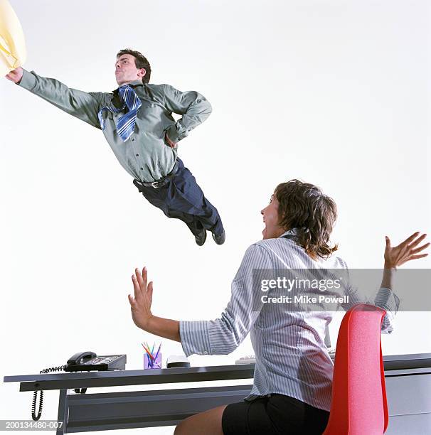 businessman flying in air, woman sitting at desk - red suit stockfoto's en -beelden