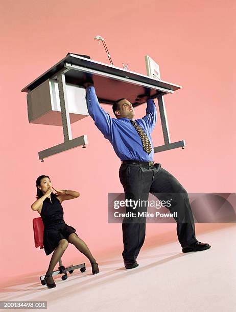 businessman lifting desk, woman with shocked expression - red shirt stockfoto's en -beelden