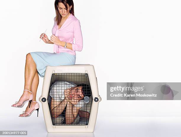woman filing nails on top of dog cage containing man - woman sitting top man stock pictures, royalty-free photos & images