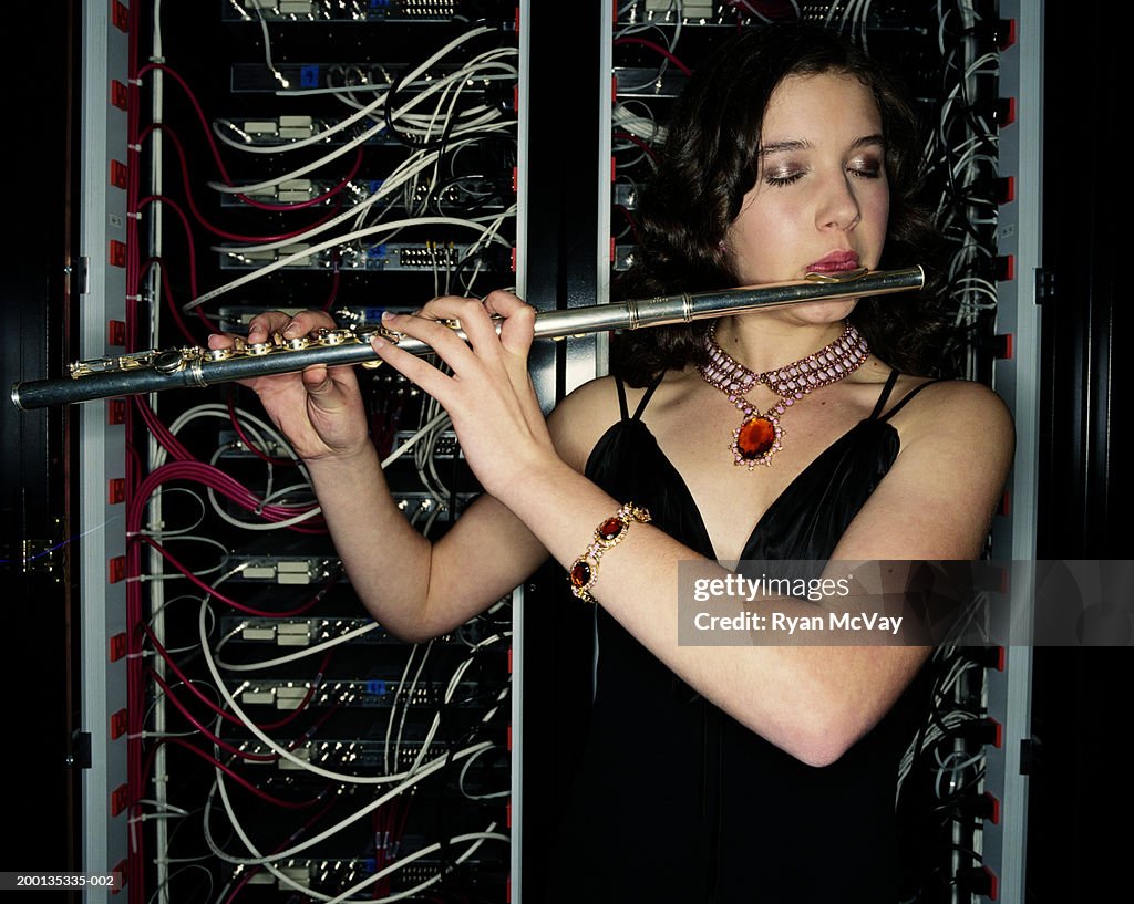 Teenage girl (16-18) playing flute, standing in server room