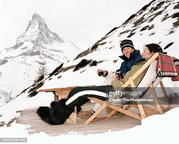 switzerland, zermatt, couple in deck chairs drinking, by matterhorn - botas de après ski fotografías e imágenes de stock