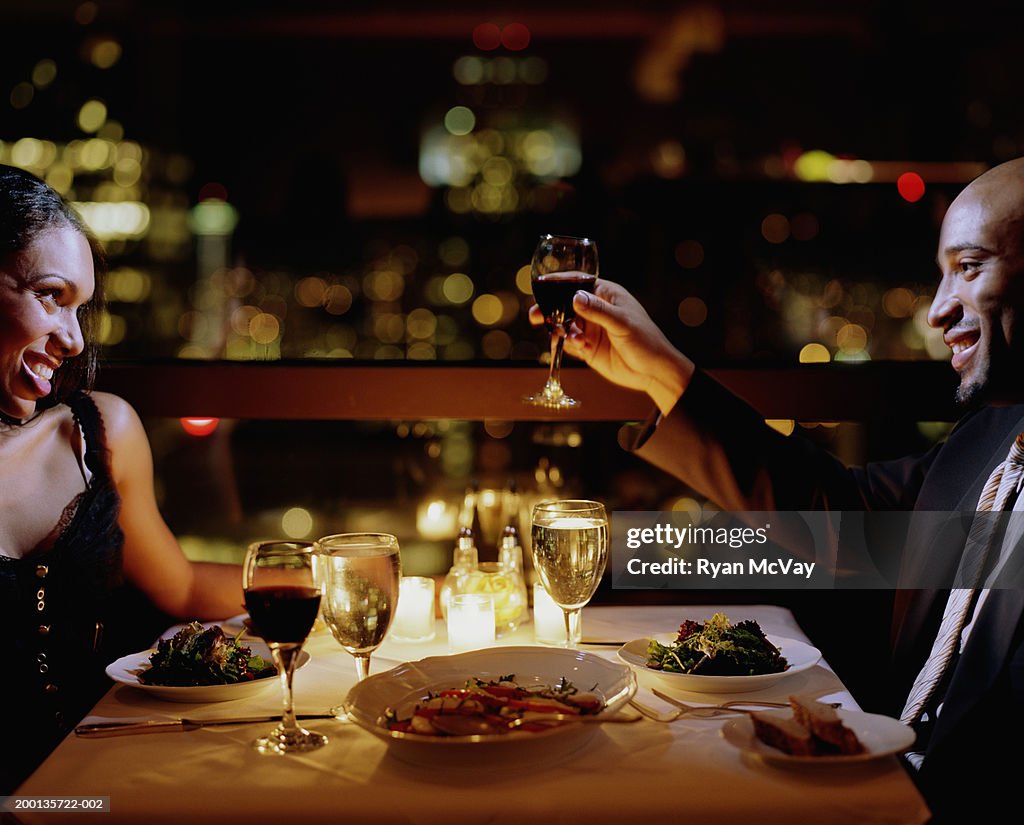 Man toasting woman at restaurant table, side view