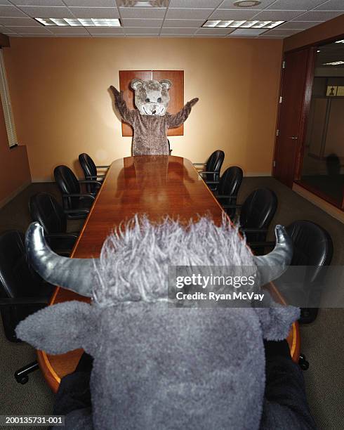 bear and bull looking at each other across conference room table - bear suit stock-fotos und bilder