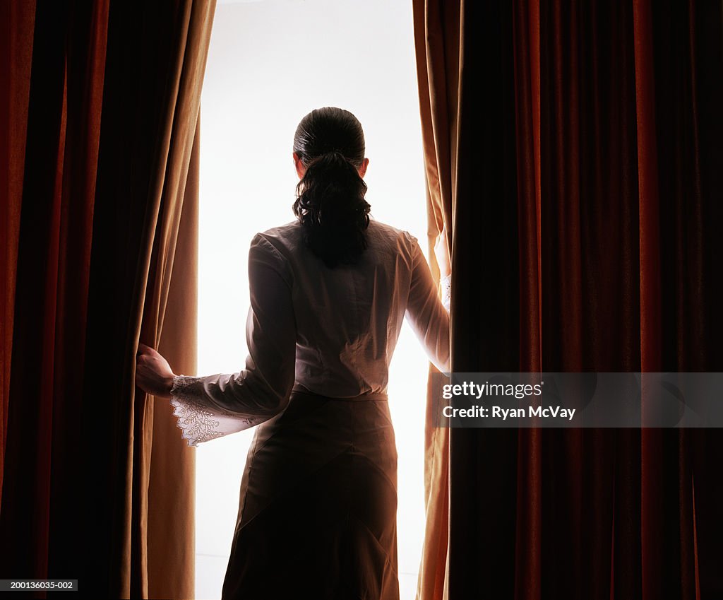 Jeune femme regardant à travers les rideaux rouge, vue de dos