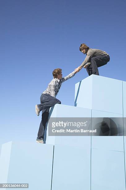 man assisting friend to climb large blocks, outdoors - 階段　のぼる ストックフォトと画像