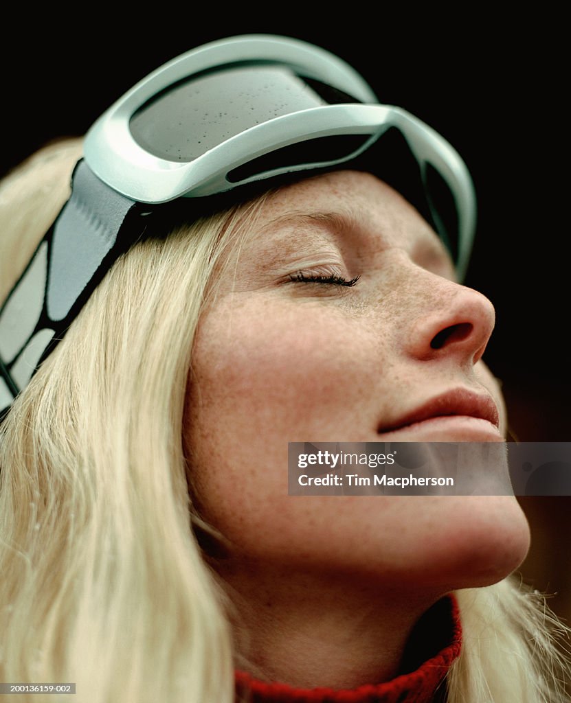 Young woman wearing ski goggles, eyes-closed, close-up