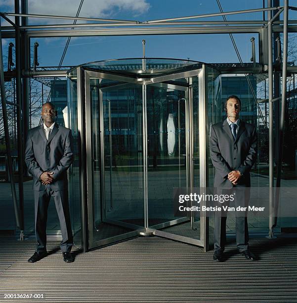 two men in suits, standing either side of revolving door, portrait - security man stock pictures, royalty-free photos & images