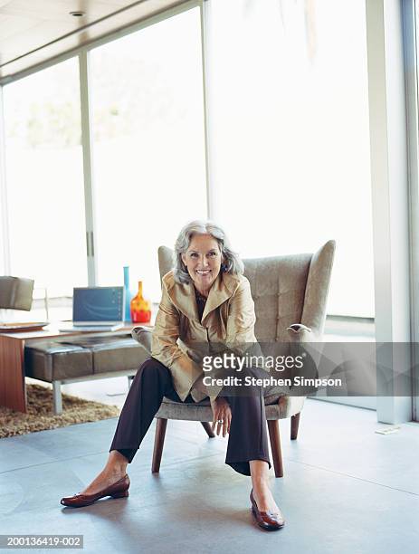 mature woman sitting on chair in house, portrait - lila schuhe stock-fotos und bilder