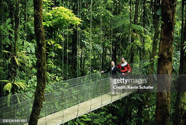 man and woman walking across footbridge in rainforest - central america stock pictures, royalty-free photos & images