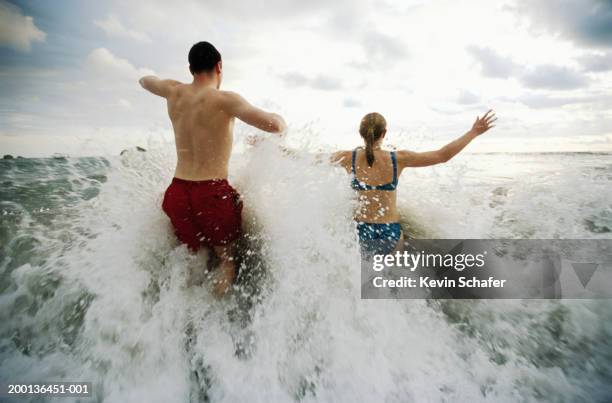 man and woman wading in surf, rear view - hüfttief im wasser stock-fotos und bilder