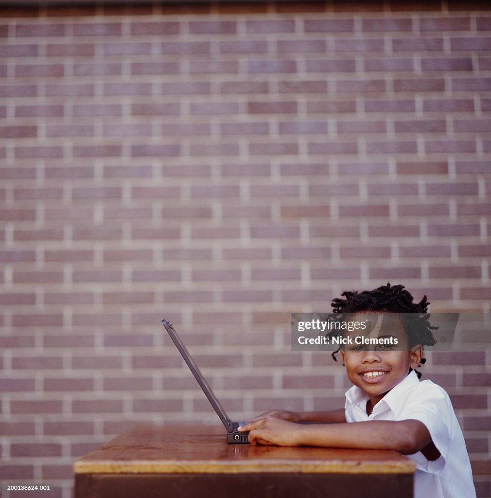 Boy (8-10) at desk with laptop, smiling, portrait
