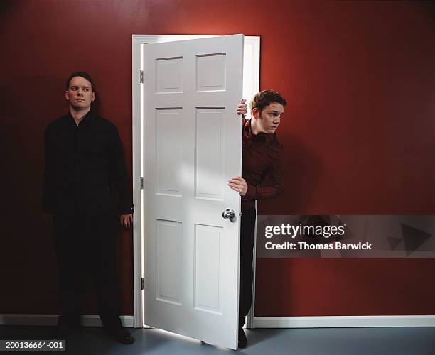 two men, one standing against wall, other peering around door - homme inquiet photos et images de collection