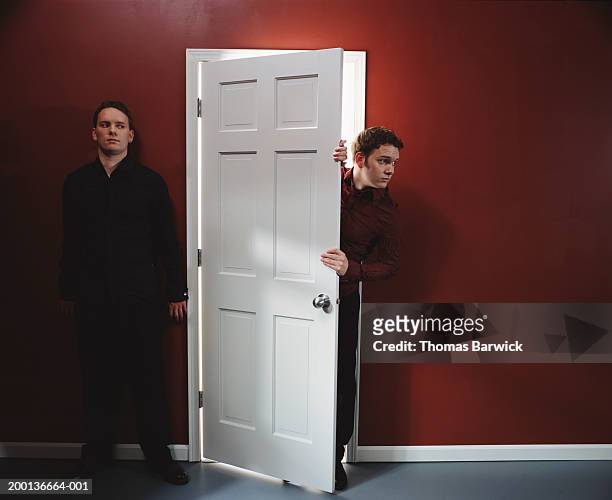 two men, one standing against wall, other peering around door - entering stock pictures, royalty-free photos & images