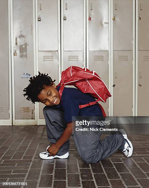 boy (8-10) kneeling, tying shoelace, smiling, lockers in background - boy tying shoes stock pictures, royalty-free photos & images