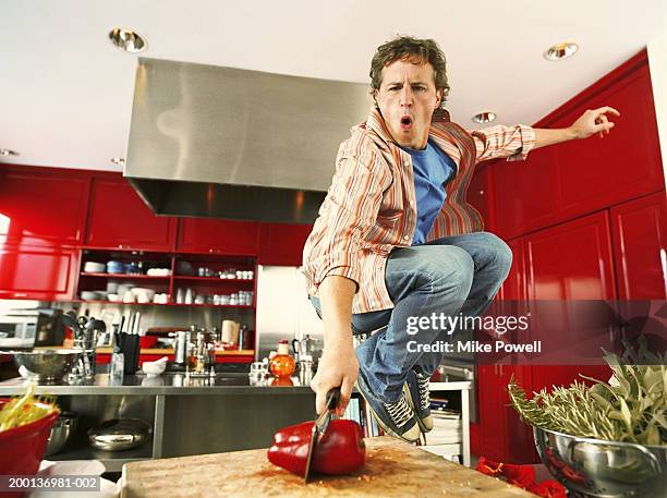 young man cutting red bell pepper in kitchen, jumping in air - bell pepper stockfoto's en -beelden