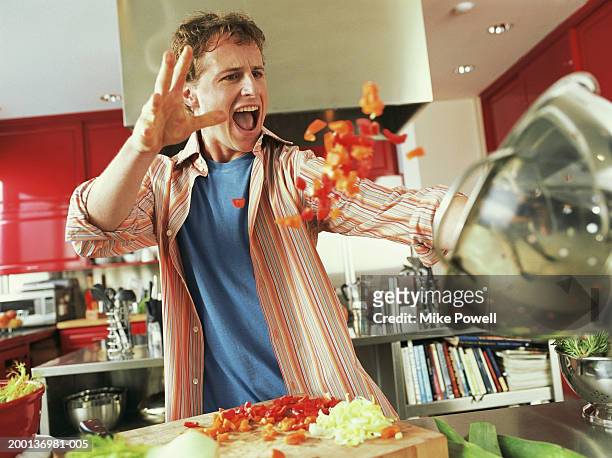 young man throwing red bell peppers into strainer - dramatisch stock-fotos und bilder