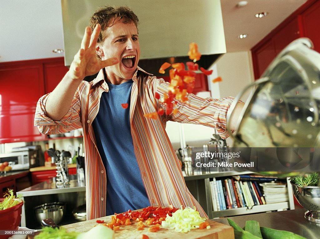 Young man throwing red bell peppers into strainer