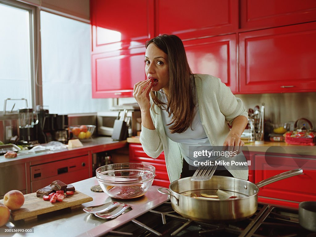 Woman eating strawberry while cooking in kitchen
