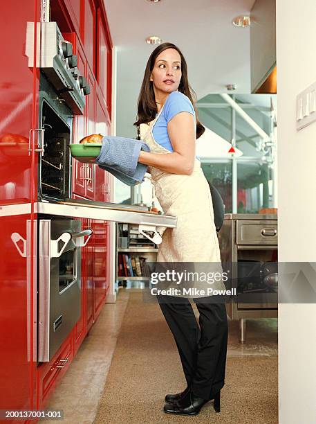 woman with kitchen mitts taking food out of oven - looking back stock-fotos und bilder