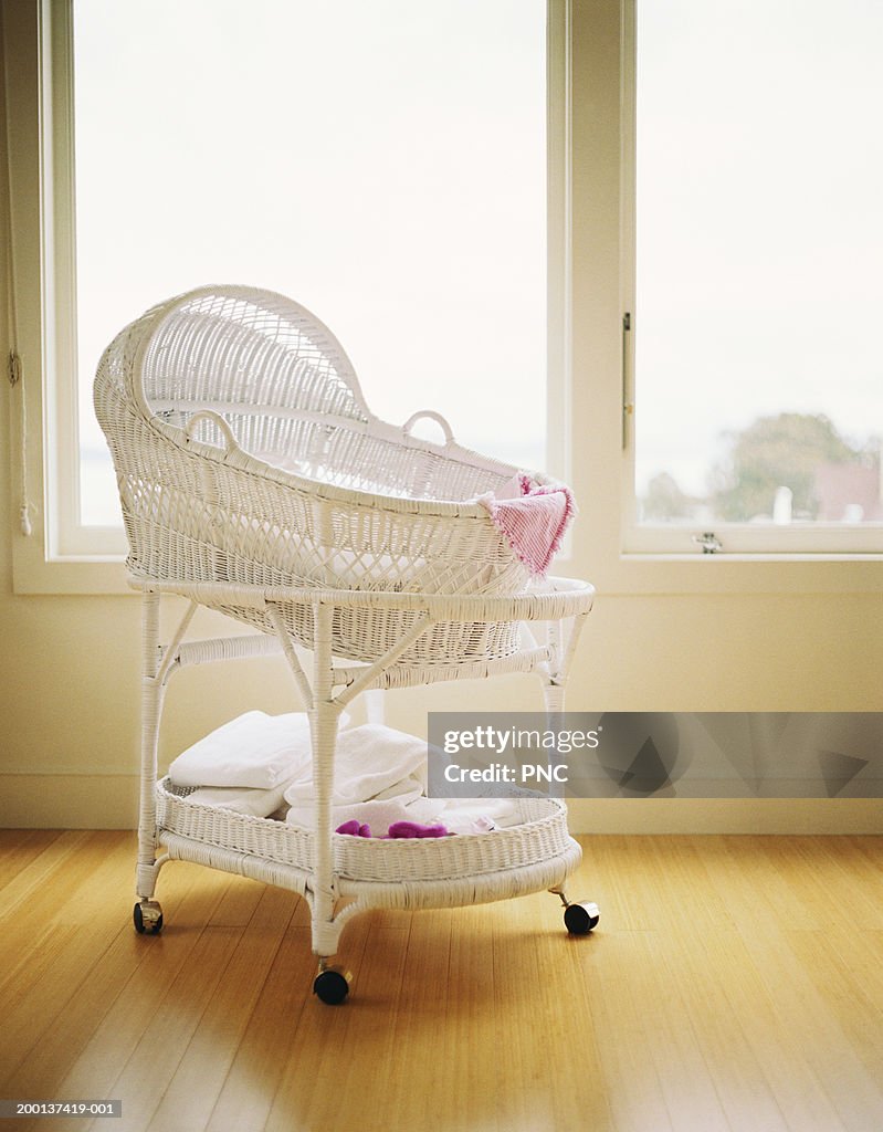 White wicker bassinet on wood floor by windows