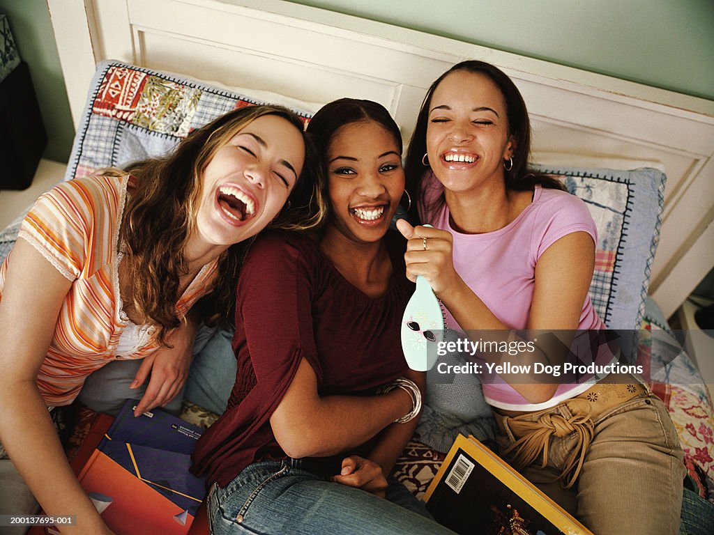 Three teenage girls (16-18) on bed laughing, elevated view