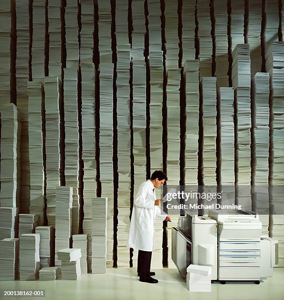 man using photocopier in front of piles of paper - kopiergerät stock-fotos und bilder