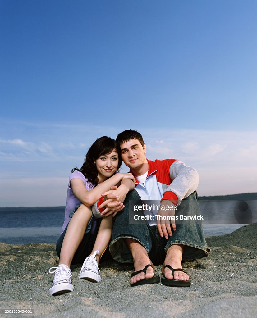 Young couple sitting on beach, holding hands, portrait