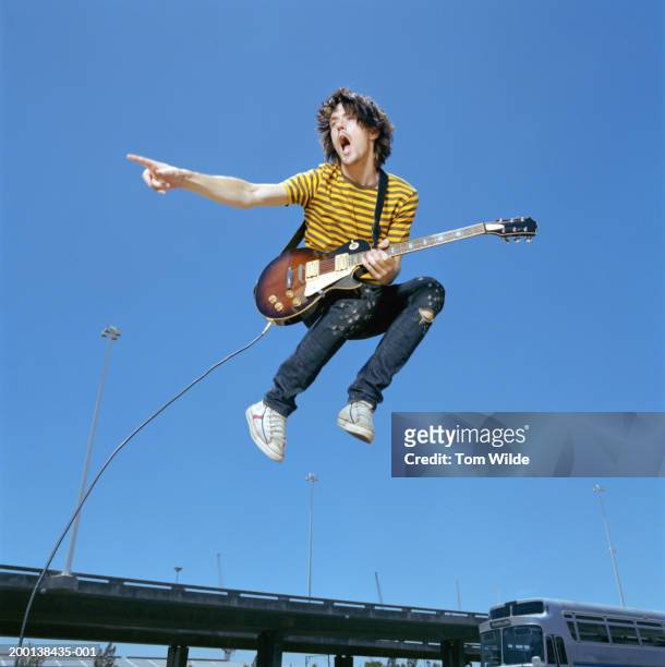 young man with guitar leaping in air outdoors, low angle view - guitarrista fotografías e imágenes de stock