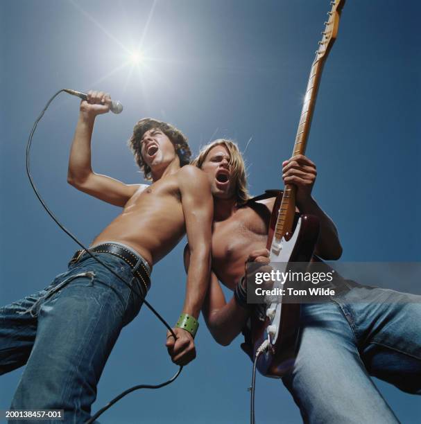 two bare chested men, one singing, one playing guitar, low angle view - rocker - fotografias e filmes do acervo