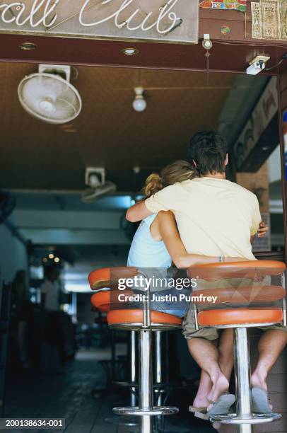 young couple embracing on bar stools, rear view - bar man t shirt ストックフォトと画像