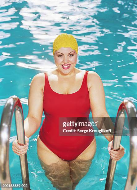 woman standing in swimming pool holding railings to steps, portrait - one piece swimsuit stock pictures, royalty-free photos & images