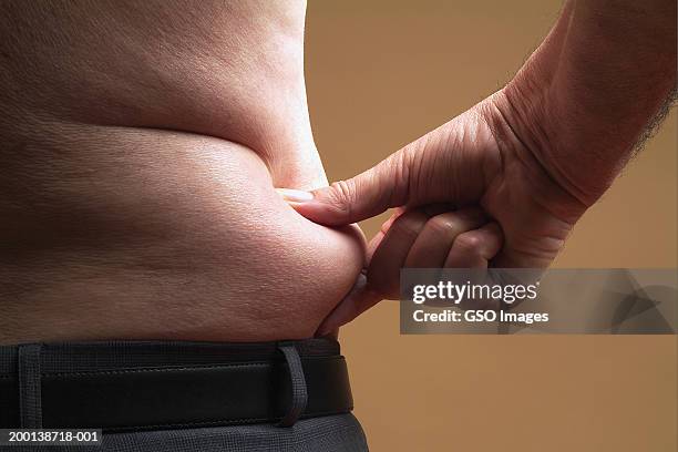 bare-chested senior man pinching skin around waist, mid section - overweight man stock pictures, royalty-free photos & images