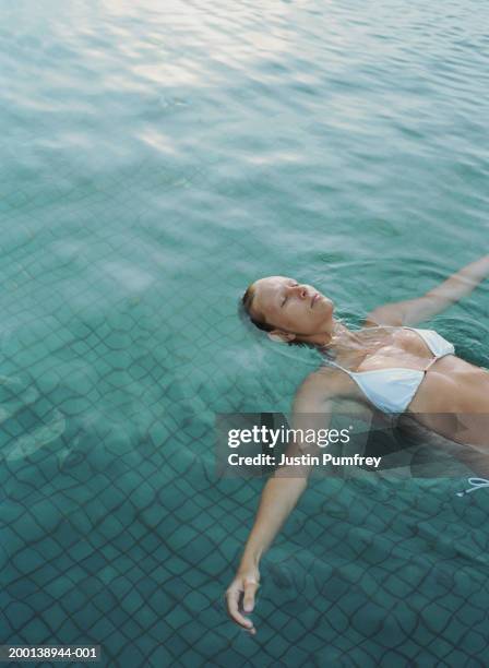 young woman floating in pool, arms outstretched, eyes closed - luxury relaxation stock pictures, royalty-free photos & images