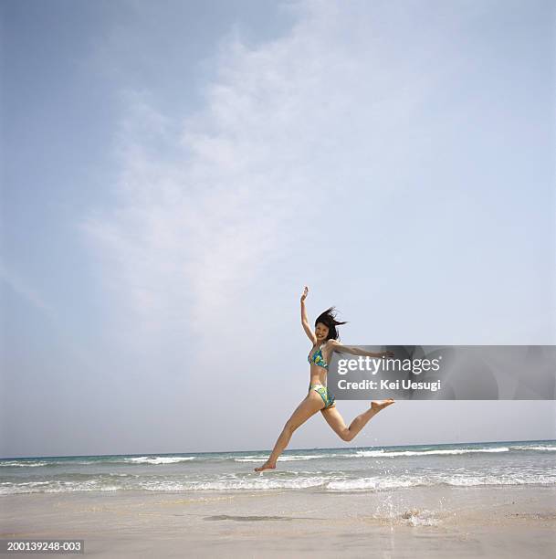 young woman leaping across beach - swimwear ストックフォトと画像