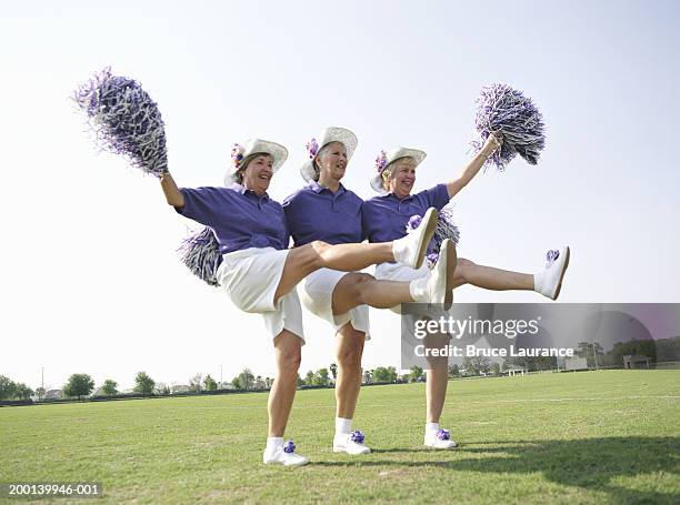 three senior women in cheerleading uniforms kicking up legs - cheerleaders stock pictures, royalty-free photos & images