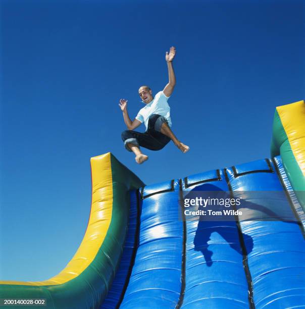 young man leaping down inflatable slide outdoors, low angle view - slide photos et images de collection