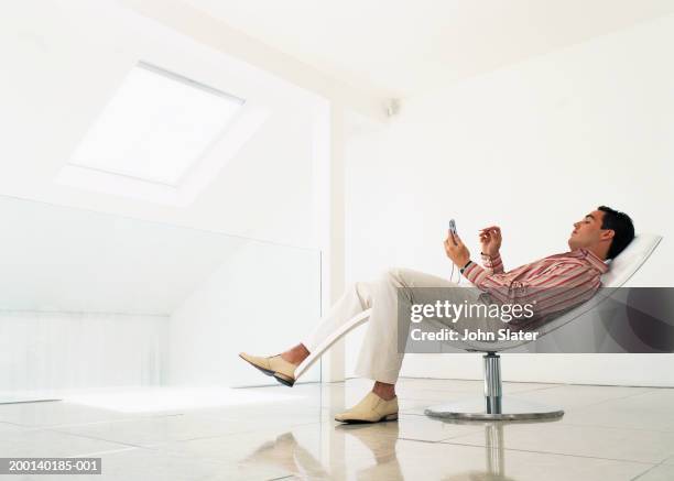 man reclining on chair using electronic organiser, side view - recliner chair stock pictures, royalty-free photos & images