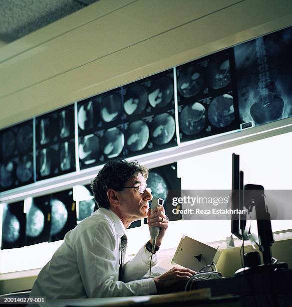 radiologist looking at computer screen, x-rays in background - radioloog stockfoto's en -beelden