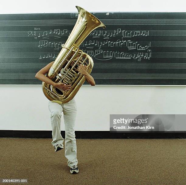 young woman struggling to hold tuba in front of music on blackboard - tube foto e immagini stock
