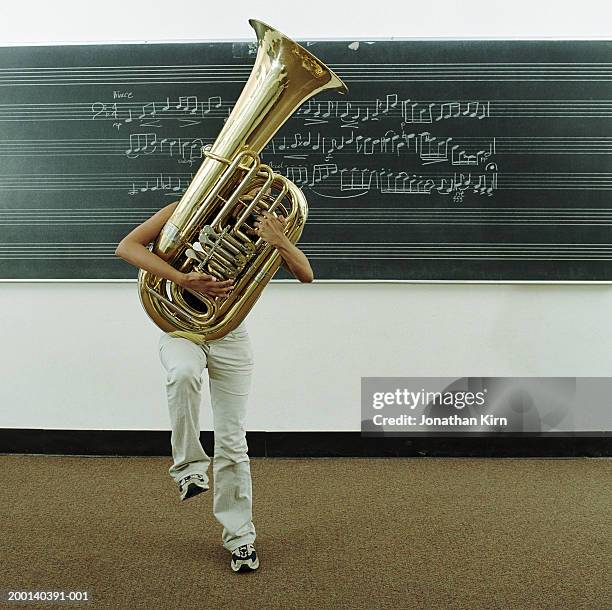 young woman struggling to hold tuba in front of music on blackboard - tuba imagens e fotografias de stock
